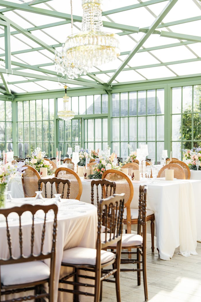 Sunlit glass venue set for an elegant wedding reception with floral decorations and chandeliers.
